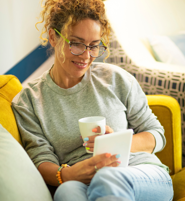Lady with glasses and curly hair sitting on a couch with a tablet device